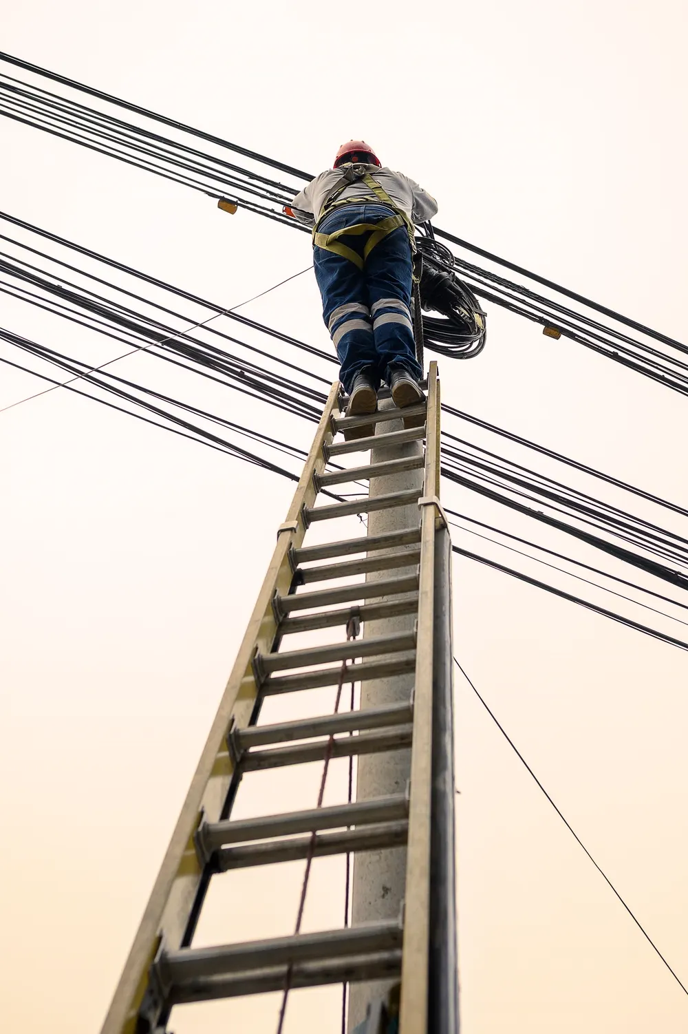 Instalador subiendo por una escalera a un poste